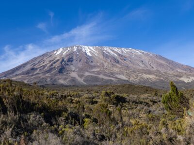 A breathtaking landscape of Mount Kilimanjaro with clear skies, showcasing the snowy peak and lush greenery.